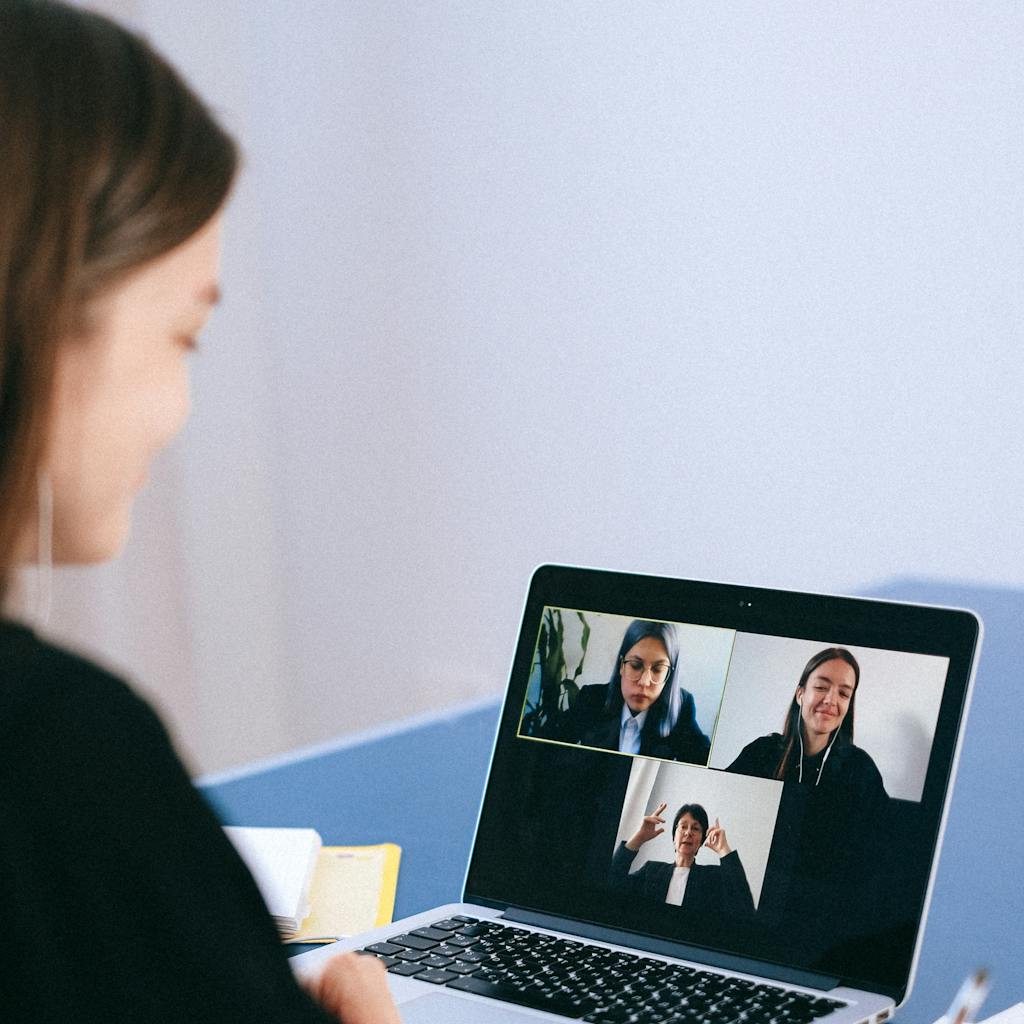 A woman participates in a virtual meeting with colleagues via video call on a laptop.