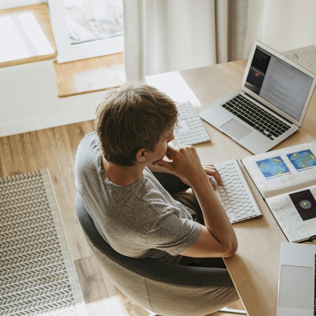 Top view of young programmer working on multiple laptops in a modern office setting.